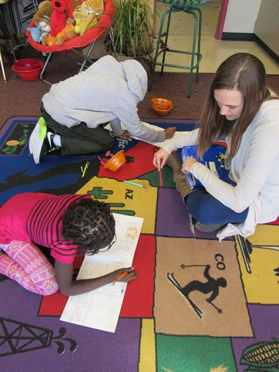 teacher and students sitting on rug while reading books